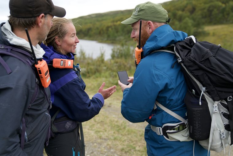 Three people looking at the app during gathering in the mountains